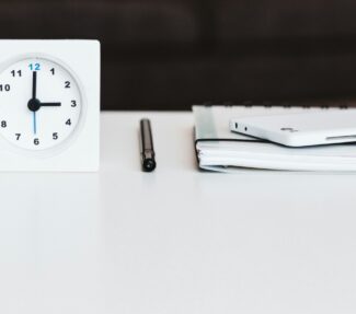 A clock, a pen and a notepad on the surface of a desk