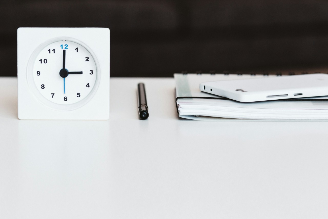 A clock, a pen and a notepad on the surface of a desk