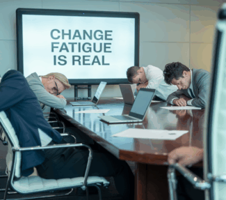 Visibly exhausted office workers around a conference table with a screen with the words "Change Fatigue is Real"