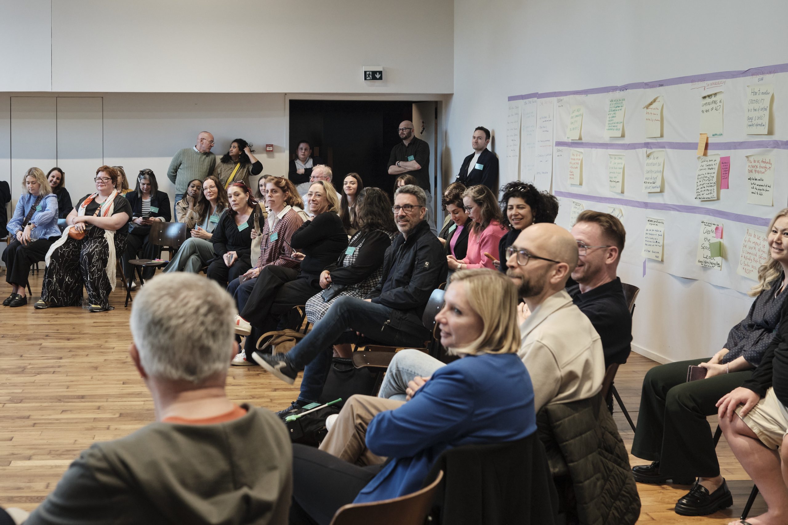 Participants at Communication Leadership Summit seated in front of wall with the Summit calendar made up of extra-large sticky notes containing proposed participation sessions.